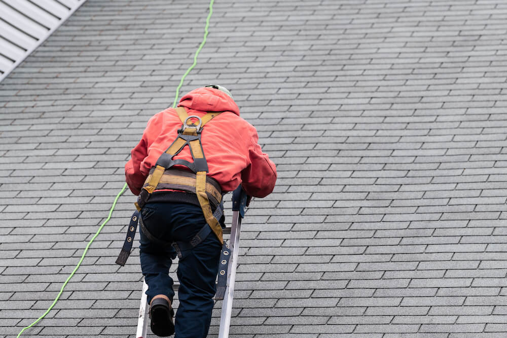 House during day with gray color Single Family Home and construction man in uniform walking on roof shingles and ladder during repair