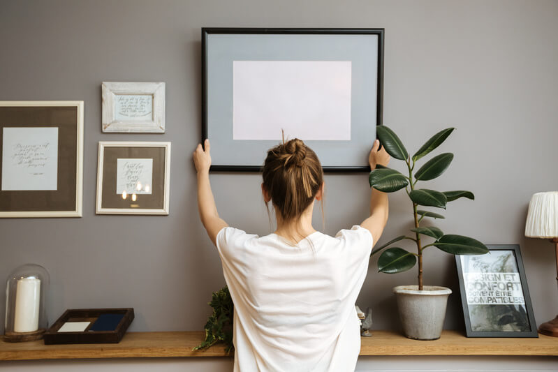 Girl remove a frame on a gray wall, sun light